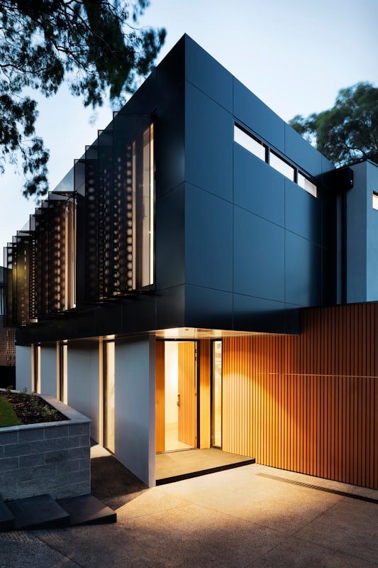The entry at night, warm light spilling from behind timber battens.