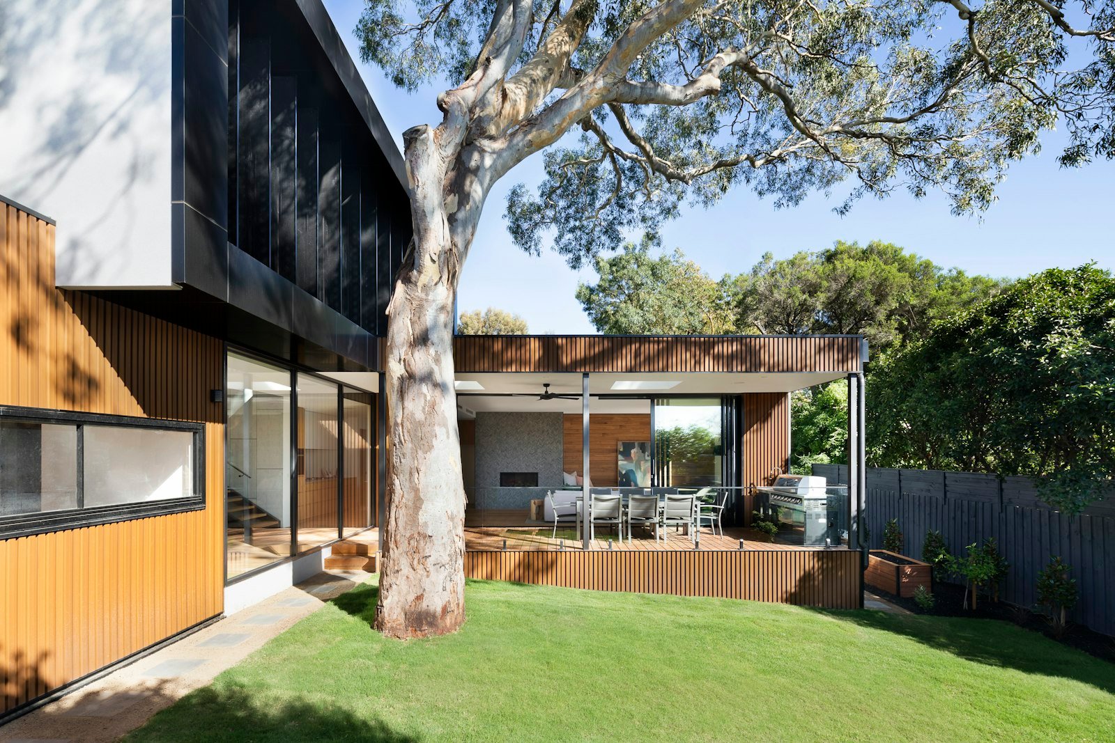 The house from the lawn, its dark timber lit from within.